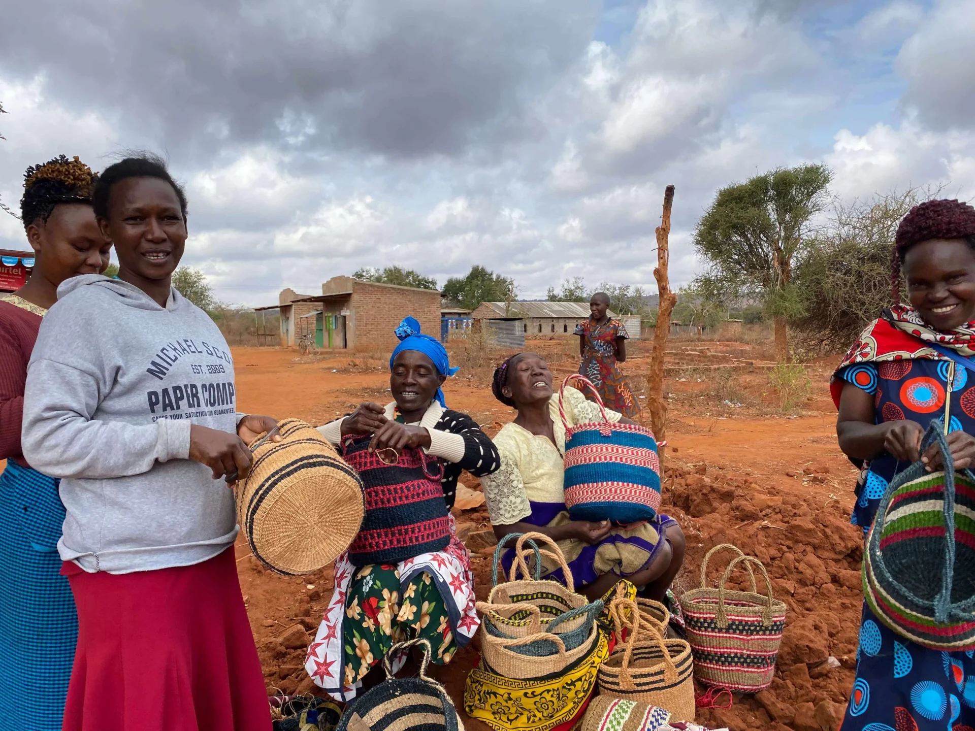 Women displaying colorful woven baskets outdoors.